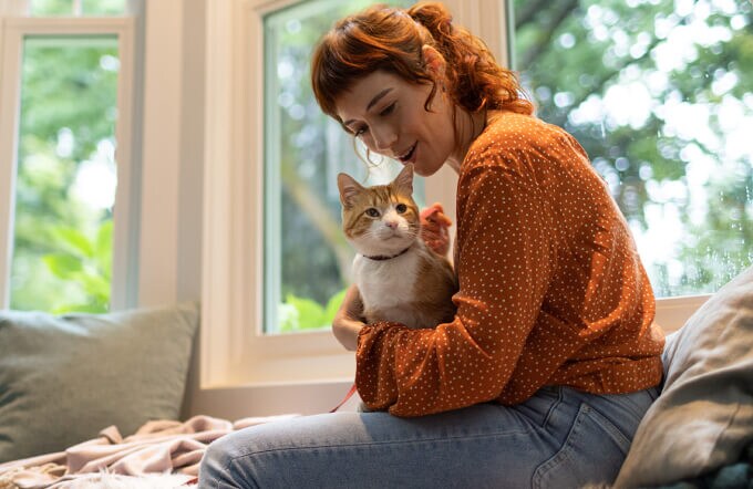Жінка в помаранчевому светрі тримає кота
